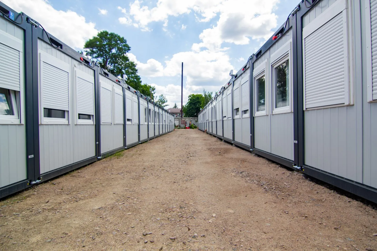 Rând de containere modulare de birou, cu ferestre și rulouri, pe un teren pietruit